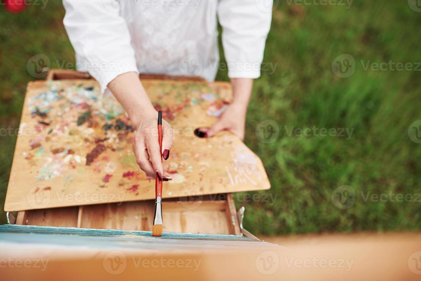 Standing outdoors. Conception of painting. Photo of woman's hand with red brush