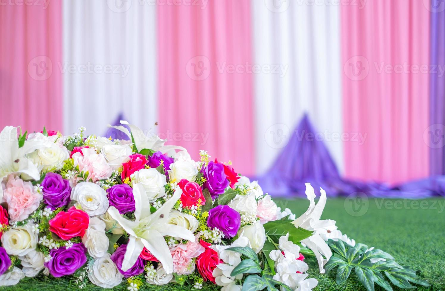 Colorful artificial bouquets placed on green artificial grass, stage cloth backdrop. photo