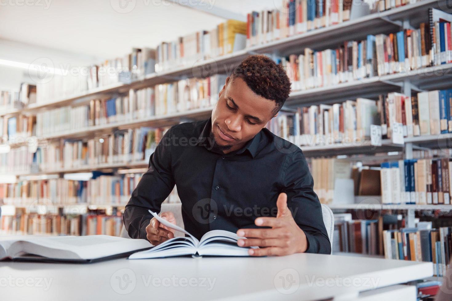 Smart student. African american man sitting in the library and searching for some information in the books photo