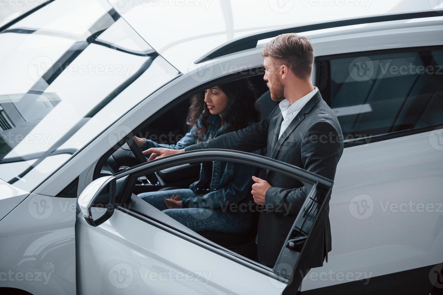 Helping girl to decide. Female customer and modern stylish bearded businessman in the automobile saloon photo