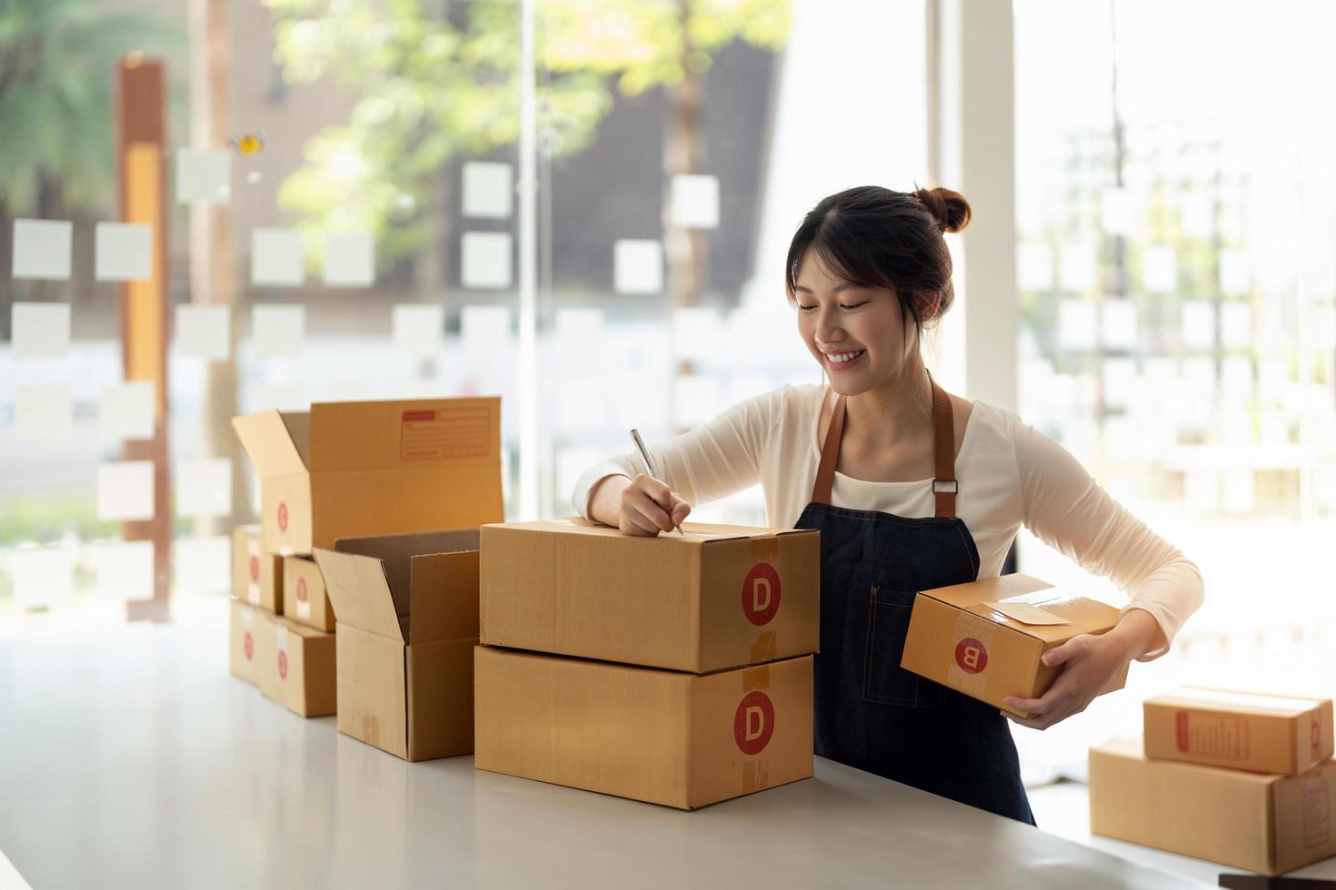 Young Asian small business owner working at home office, taking note on purchase orders. Online marketing packaging delivery, startup SME entrepreneur or freelance woman concept photo