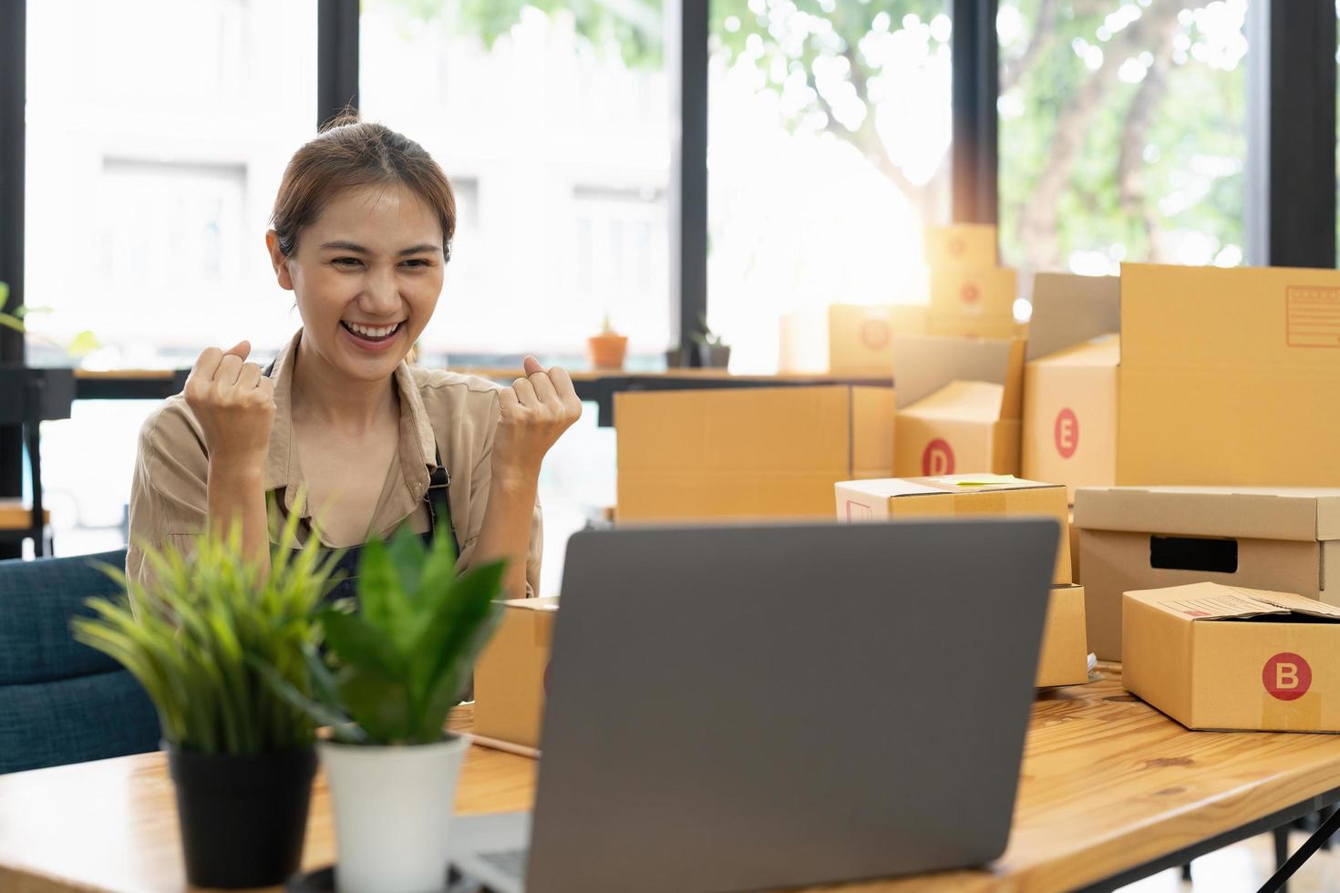 feliz joven empresaria asiática, sonríe por el éxito de las ventas después de revisar el pedido de la tienda de compras en línea en un teléfono inteligente en la oficina del hogar, concepto de negocio comercial en línea y comercio electrónico foto