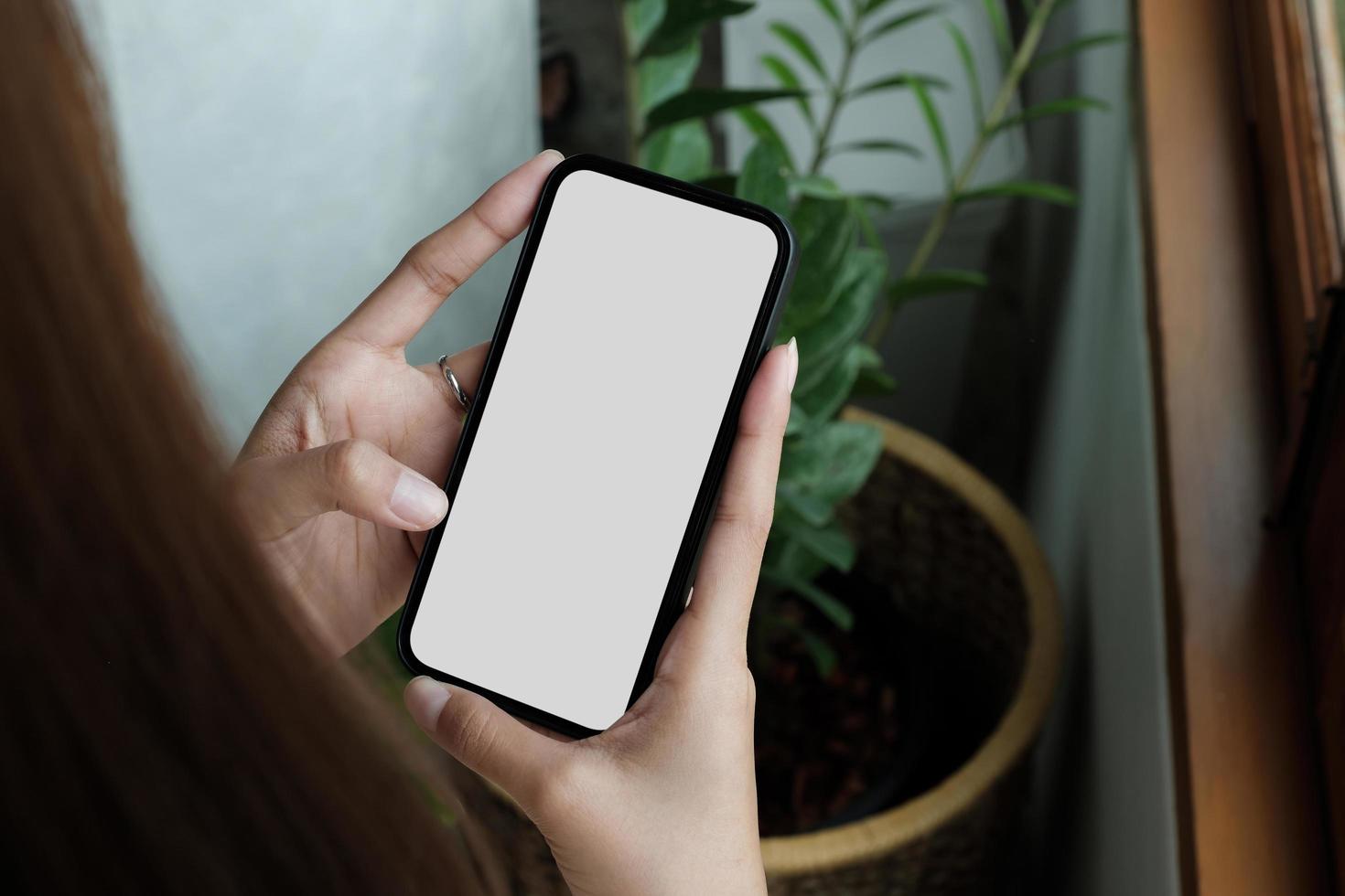 maqueta de pantalla blanca en blanco de teléfono celular. mano de mujer sosteniendo mensajes de texto usando el móvil en el escritorio en la oficina. espacio vacío de fondo para publicidad foto