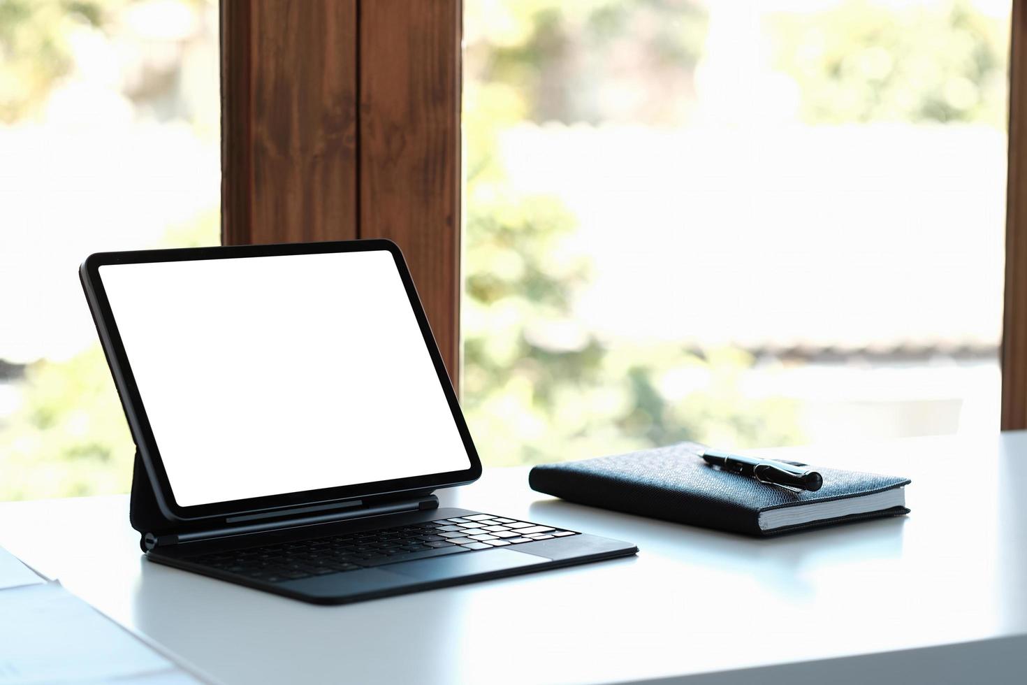 mockup image of black digital tablet pc with blank desktop white screen on working space at home office photo