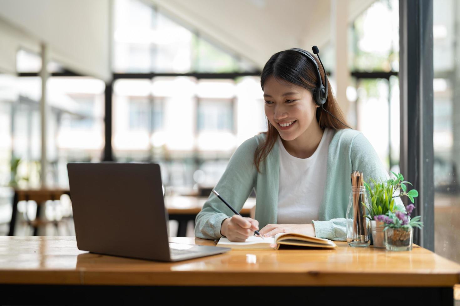 joven mujer asiática escribiendo haciendo una lista tomando notas en el bloc de notas trabajando o aprendiendo en una computadora portátil en el interior: curso educativo o capacitación, seminario, concepto de educación en línea foto