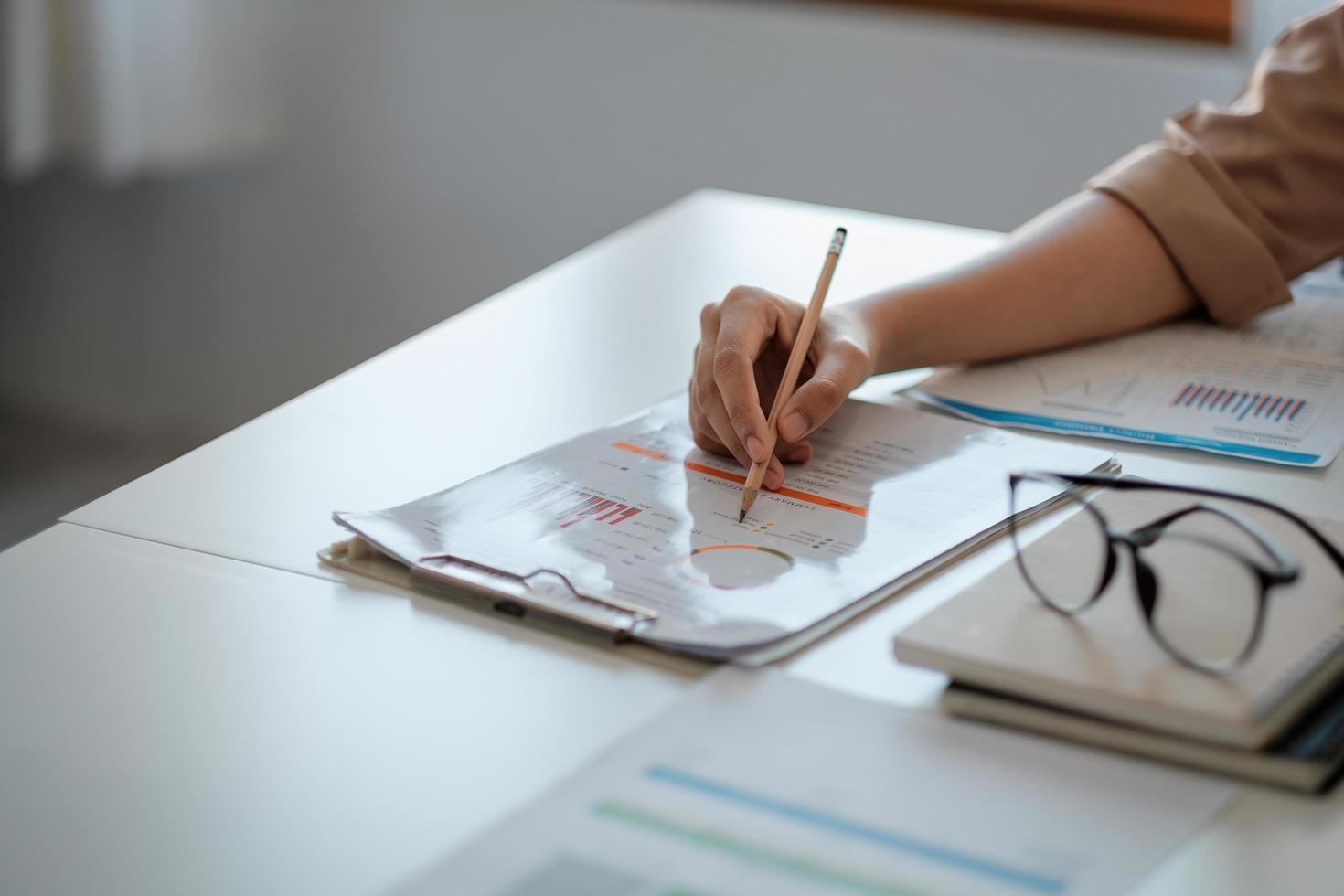Close up hand of business woman analyst pointing with pencil paperwork graph chart at work photo