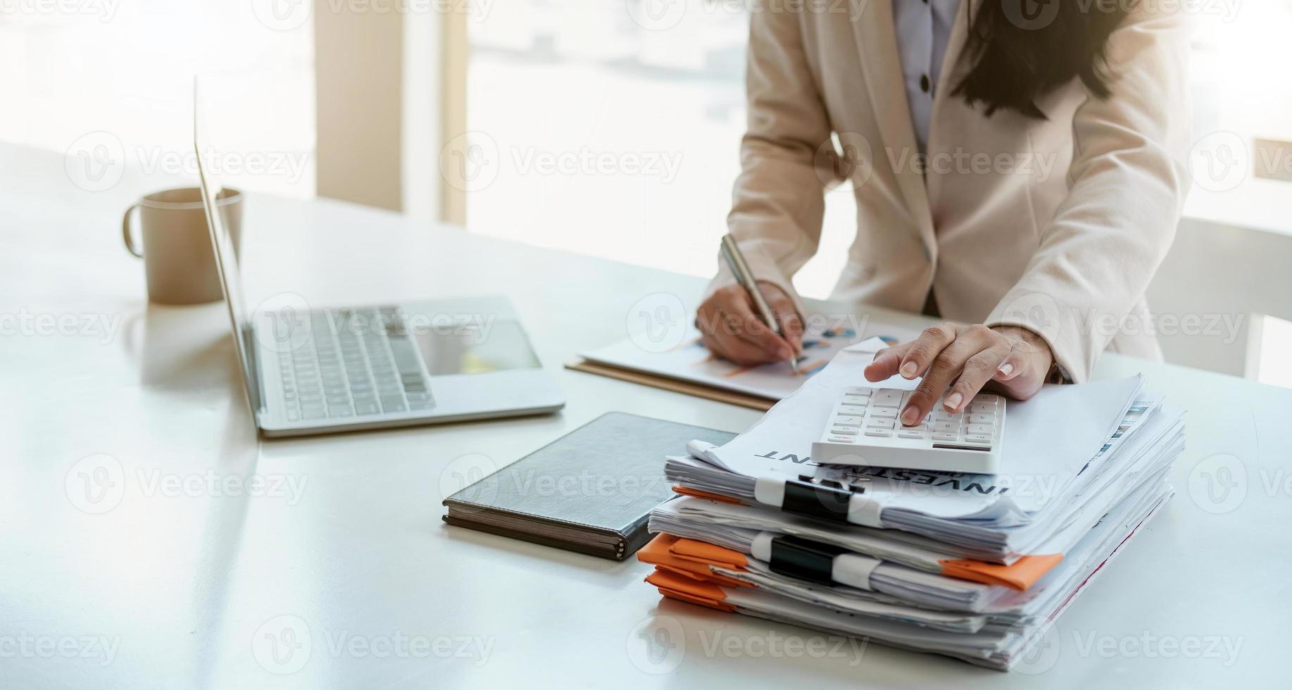 Close up of businesswoman or accountant hand holding pen working on calculator to calculate business data, accountancy document and laptop computer at office, business concept photo