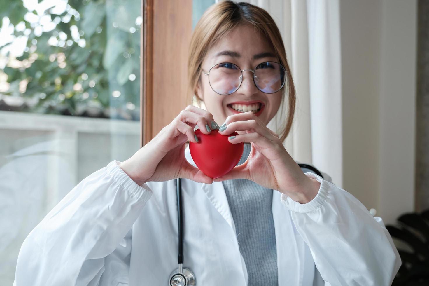 Portrait young asian beautiful doctor with stethoscope holding heart while standing at her office. photo