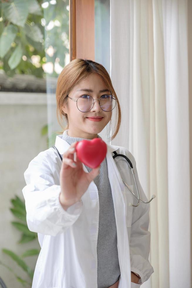 Portrait young asian beautiful doctor with stethoscope holding heart while standing at her office. photo