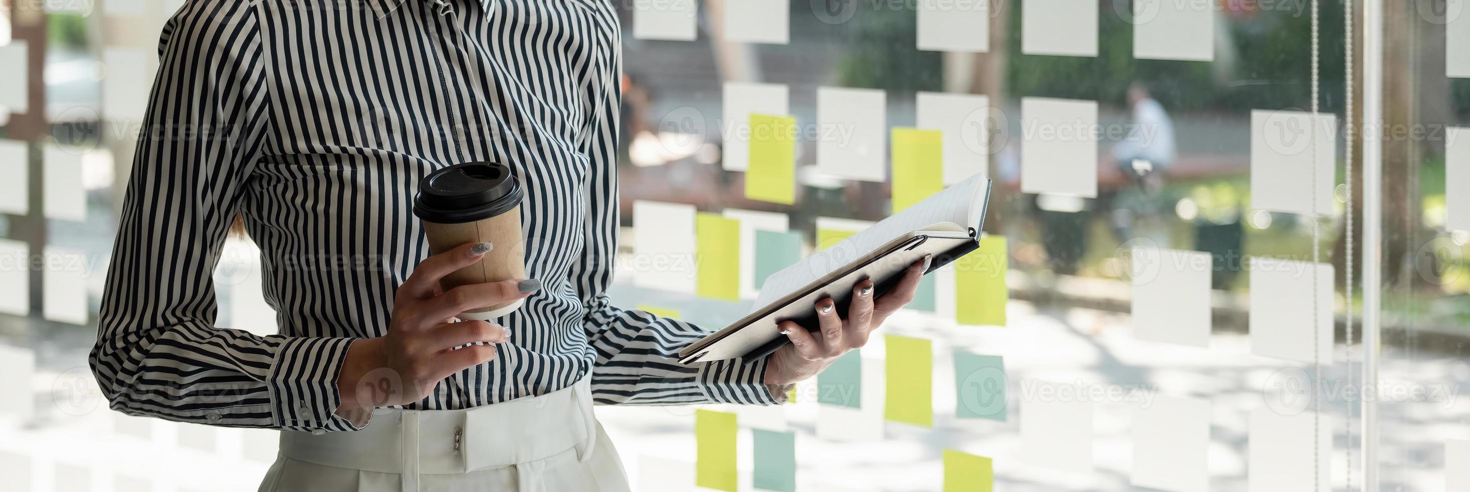 Close up business woman reading a book and writing notes while standing near window. photo