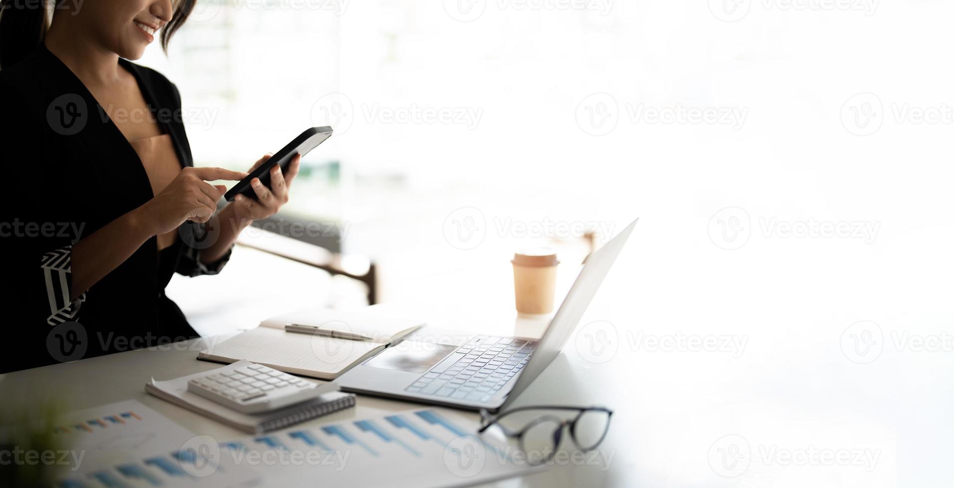 Asian woman holding smart phone while using calculator and laptop for business financial accounting calculate money bank loan rent payments manage expenses finances taxes doing paperwork concept photo