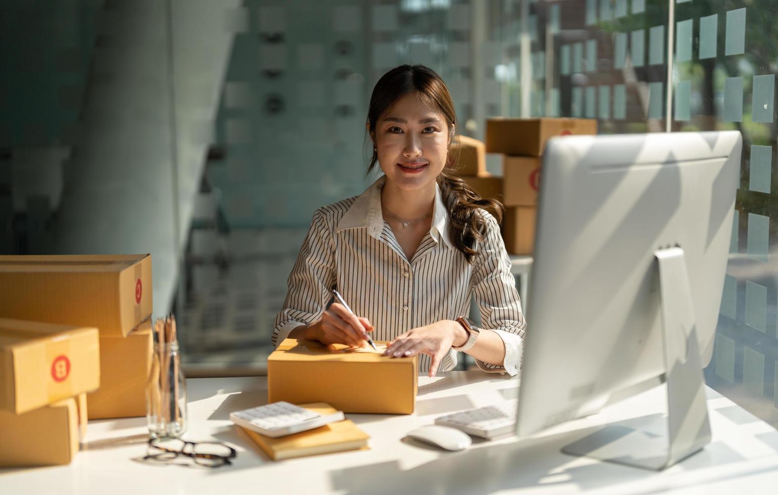 joven propietario de una pequeña empresa asiática que trabaja en la oficina de su casa, tomando nota de las órdenes de compra. entrega de empaques de marketing en línea, empresaria de pymes emergentes o concepto de mujer independiente foto