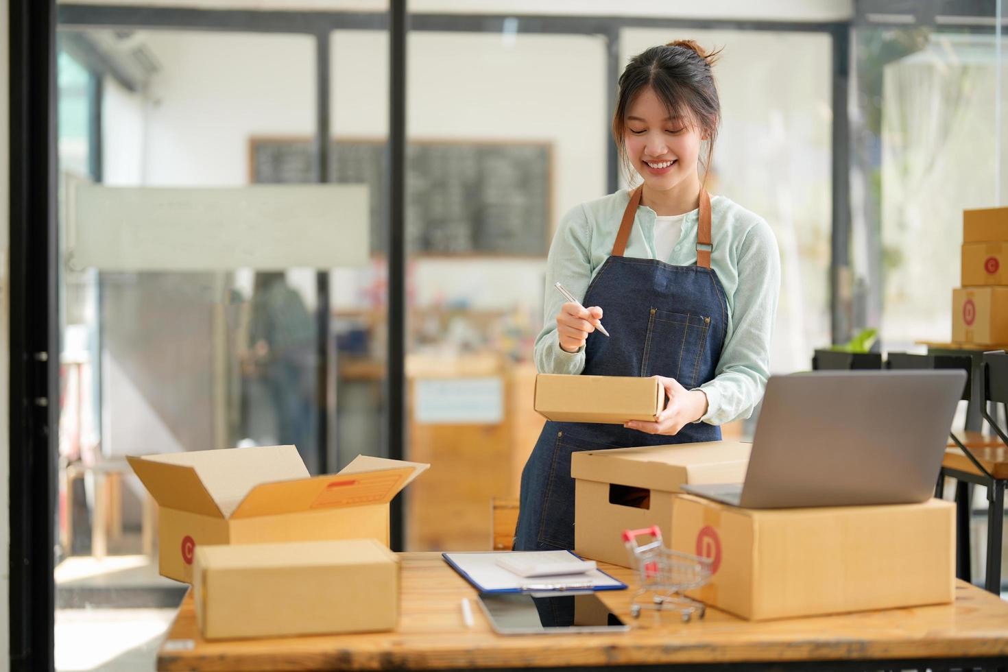 Startup small business SME, Entrepreneur owner using laptop computer taking receive and checking online purchase shopping order to preparing pack product box. Selling online ideas concept photo