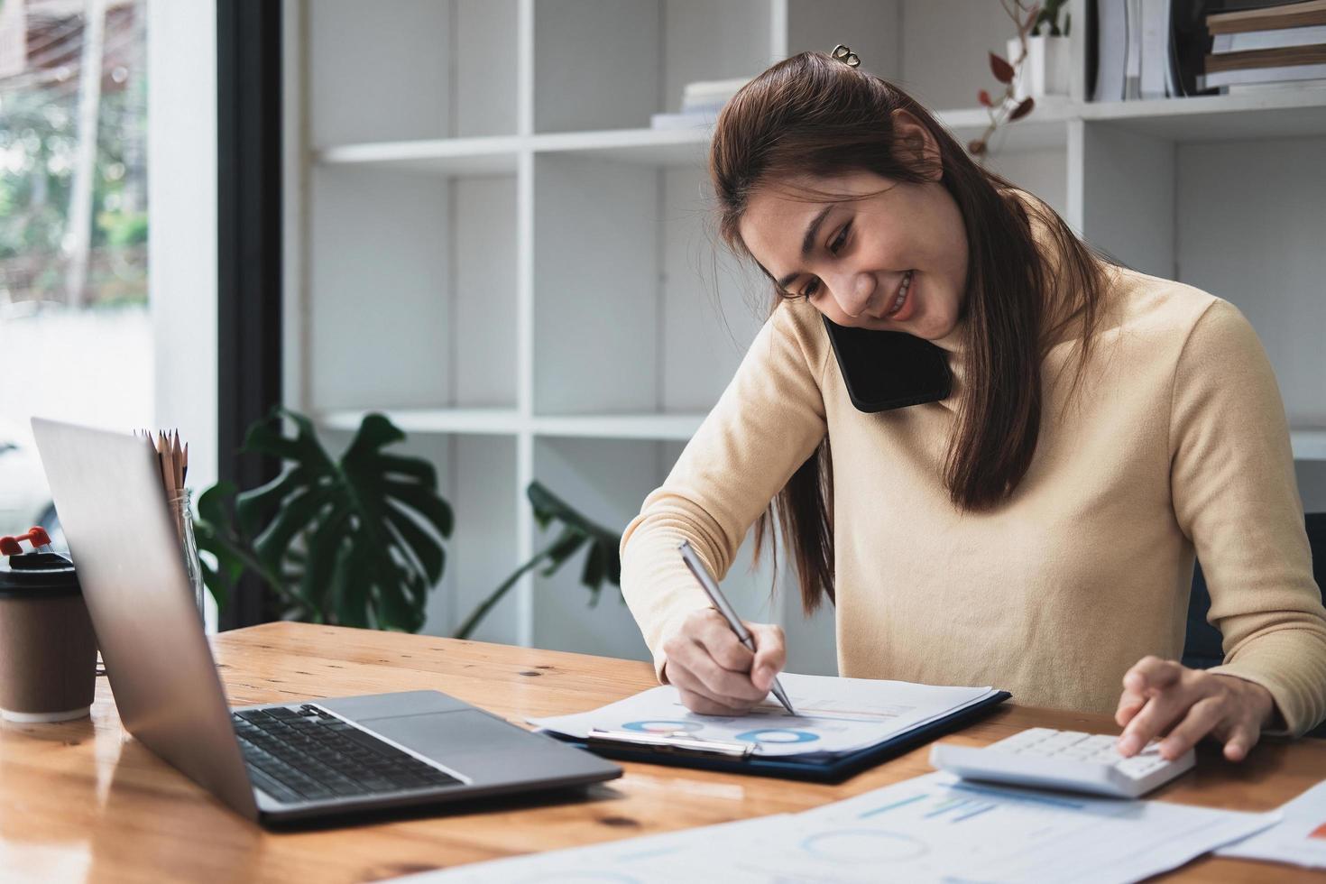 Asian business woman making a phone call, Accountant working Financial investment on calculator with calculate Analyze business and market growth on financial document data graph and writing. photo