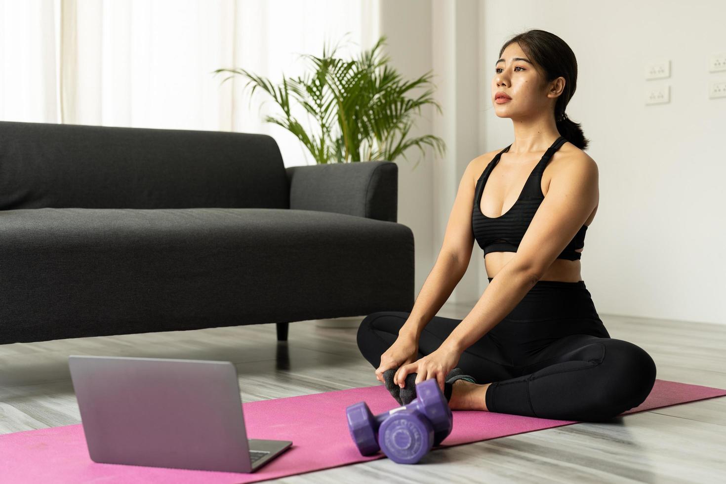 Beautiful young asian woman practicing yoga watching videos on laptop at home - Fitness, workout concept photo