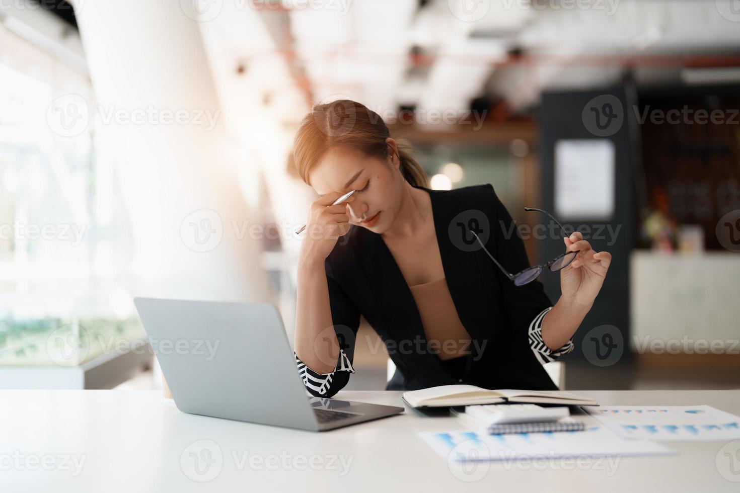 Very stressed business asian woman sitting in front of her computer looking at a large pile of paperwork, while holding a hand at her forehead photo