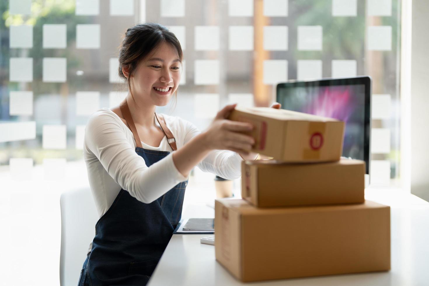 Business woman owner holding parcel box for delivery and using smartphone at home office. Entrepreneur small business working at home photo