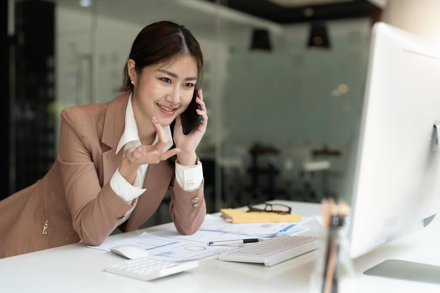 Asian accountant using smartphone to call marketing consultants and using laptop computer to analyze sales growth in the global workplace market. accounting concept photo