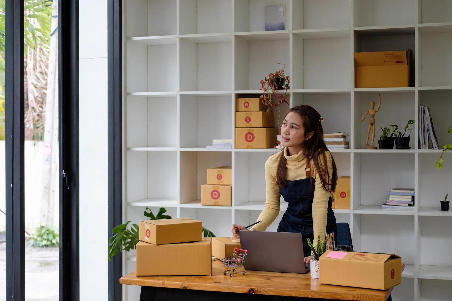 Start up small business entrepreneur SME or freelance asian woman using laptop with box, Young success Asian woman with her hand lift up , online marketing packaging box and delivery, SME concept photo