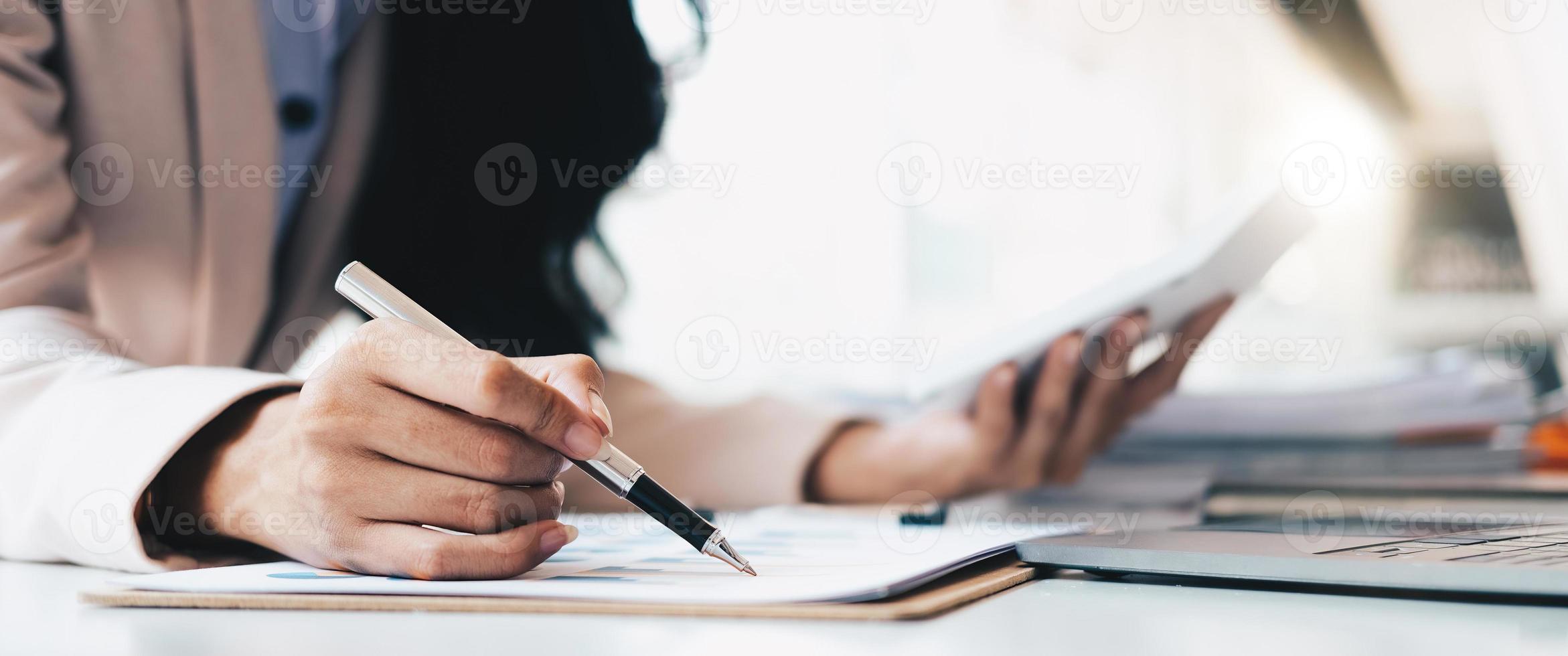 businesswoman or accountant pen pointing on graph chart while using calculator to calculate income tax and corporate income in office photo