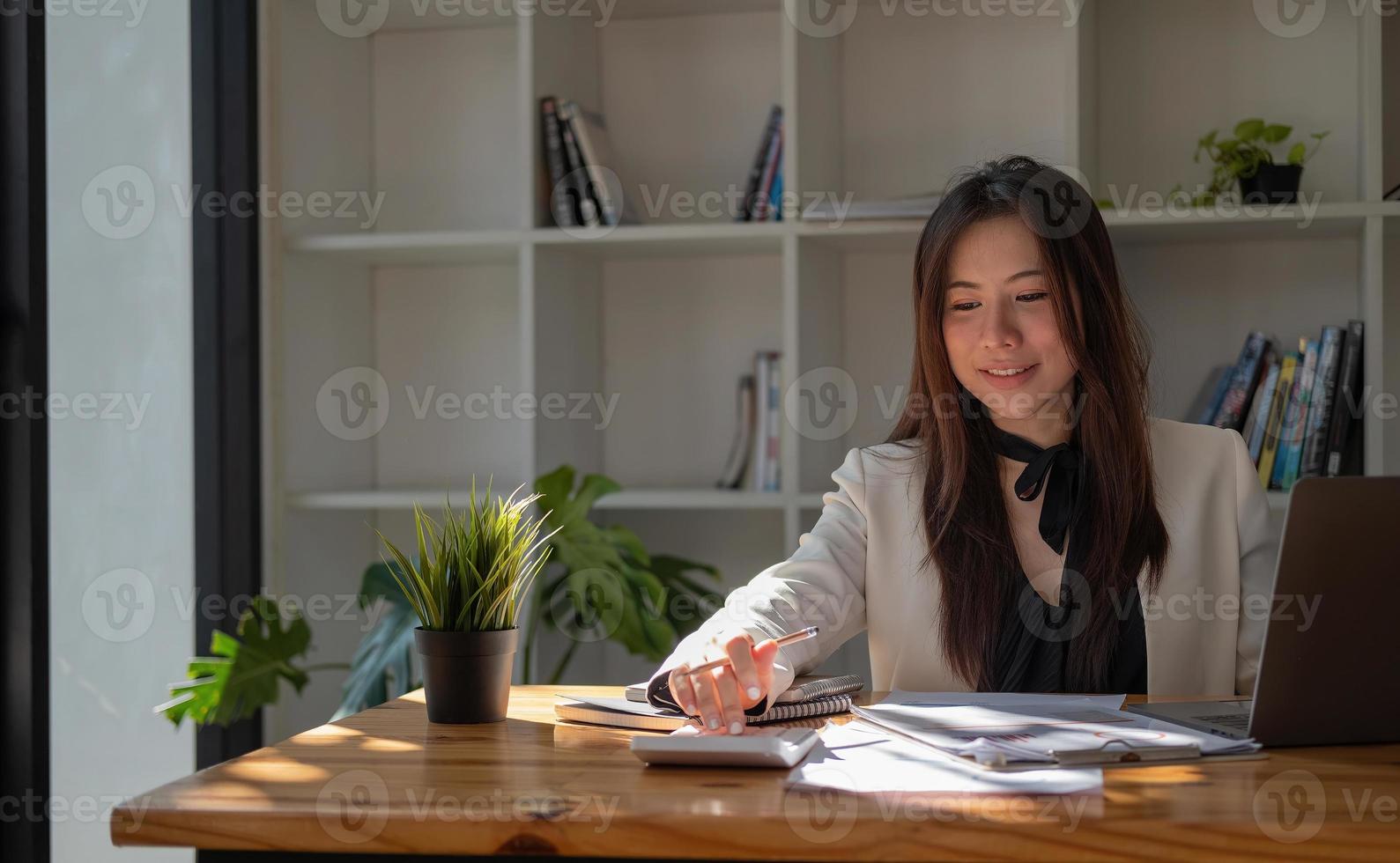 Close up of business asian woman or accountant hand holding pen working on calculator to calculate business data, accountancy document and laptop computer at office, business concept. photo