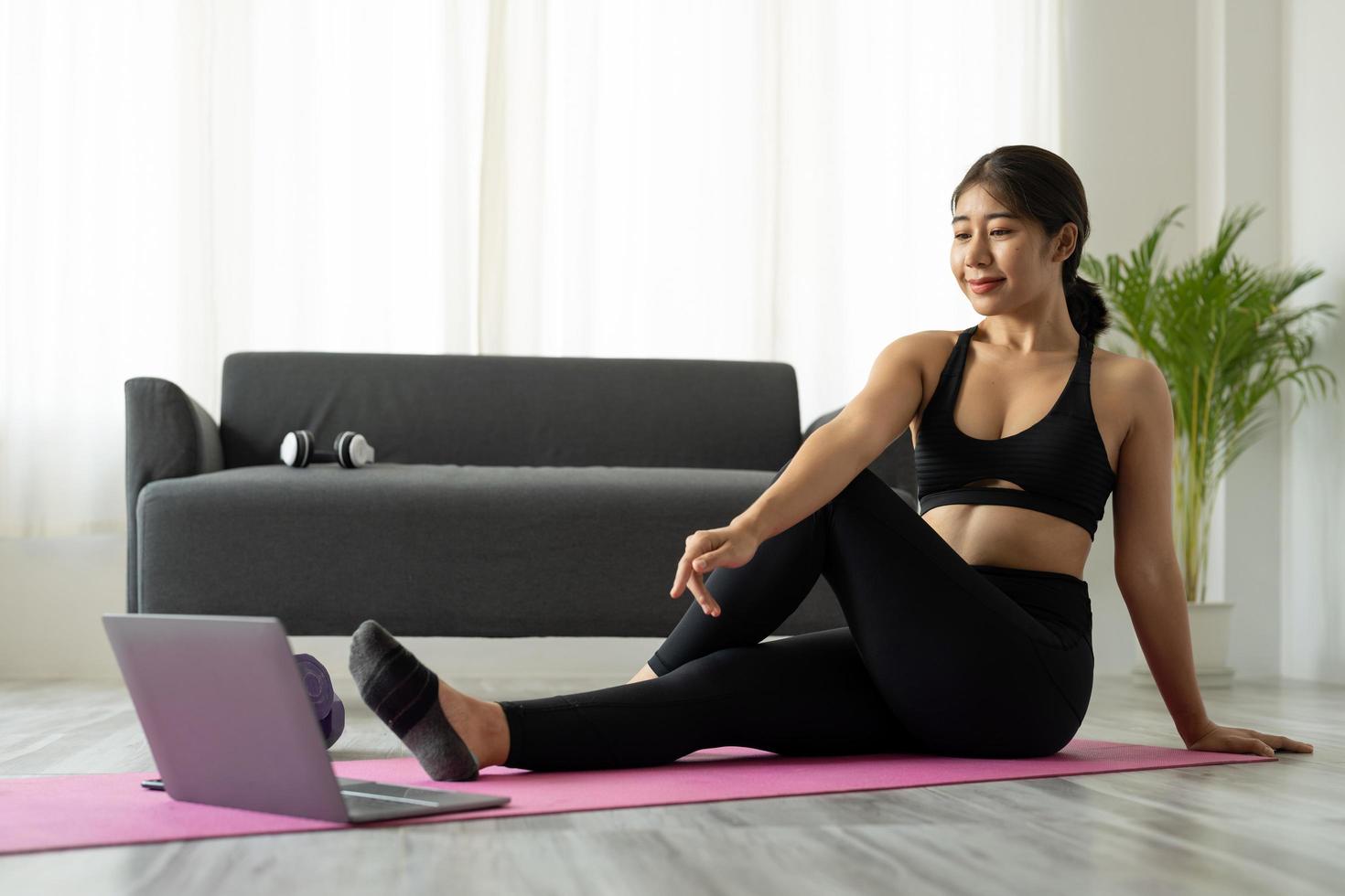 Fit sporty young asian woman online workout exercise at home. Active healthy girl enjoy sport pilates yoga fitness training on laptop computer stretching on yoga mat watching video class photo