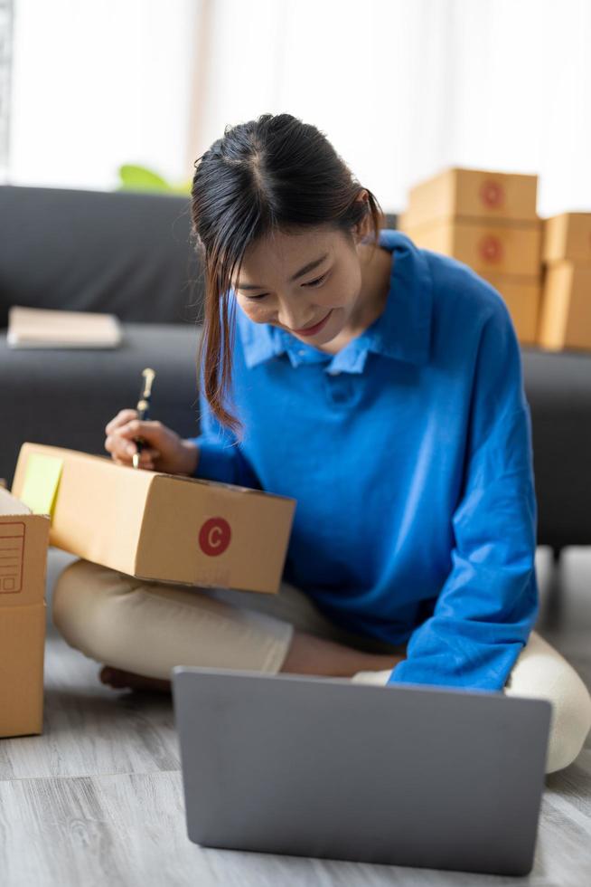 Shipping shopping online, startup small business owner writing address on cardboard box at workplace. Freelance Asian woman small business entrepreneur SME working with box at home photo