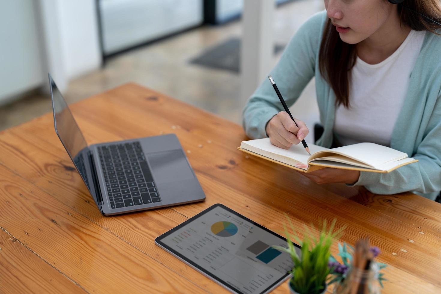Asian woman writing making list taking notes in notepad working or learning on laptop indoors- educational course or training, seminar, education online concept photo