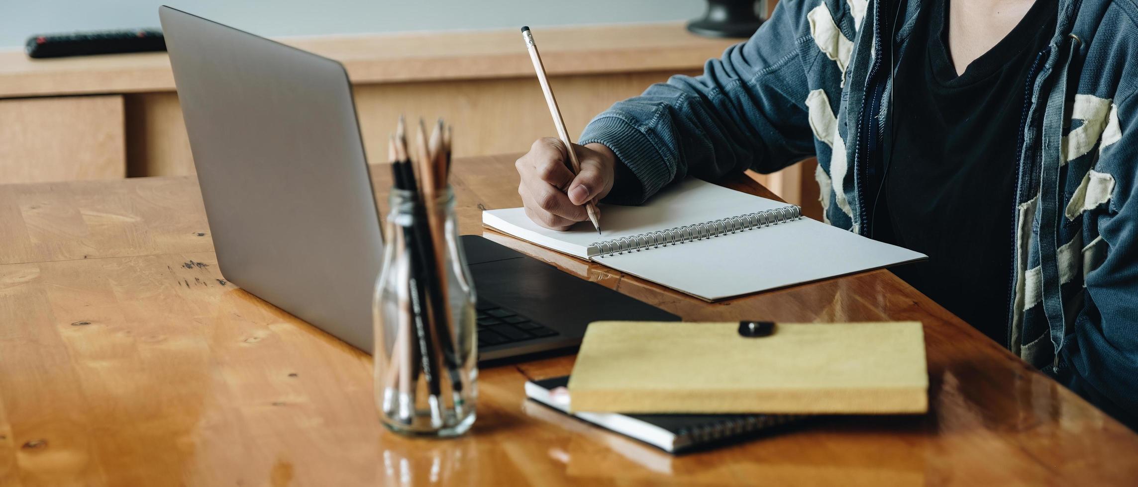 Cropped photo of woman writing making list taking notes in notepad working or learning on laptop indoors- educational course or training, seminar, education online concept