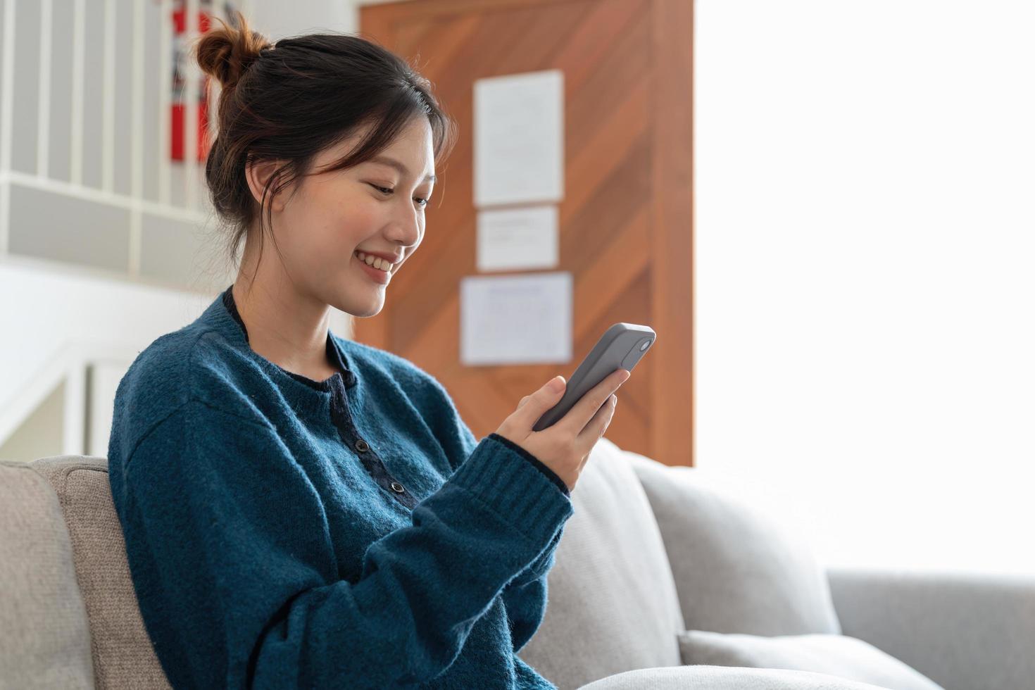 atractiva mujer sonriente usando un teléfono inteligente mientras se sienta en el sofá en casa. concepto de comunicación y comodidad foto