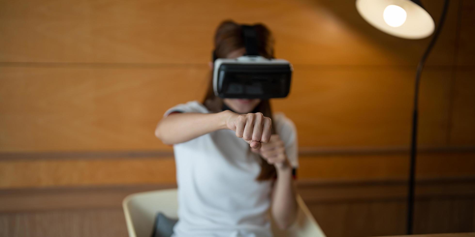 Girl wearing virtual reality glasses on head playing fighting game, holding clenched fists up ready to boxing, experiencing cyberspace using VR headset technology photo