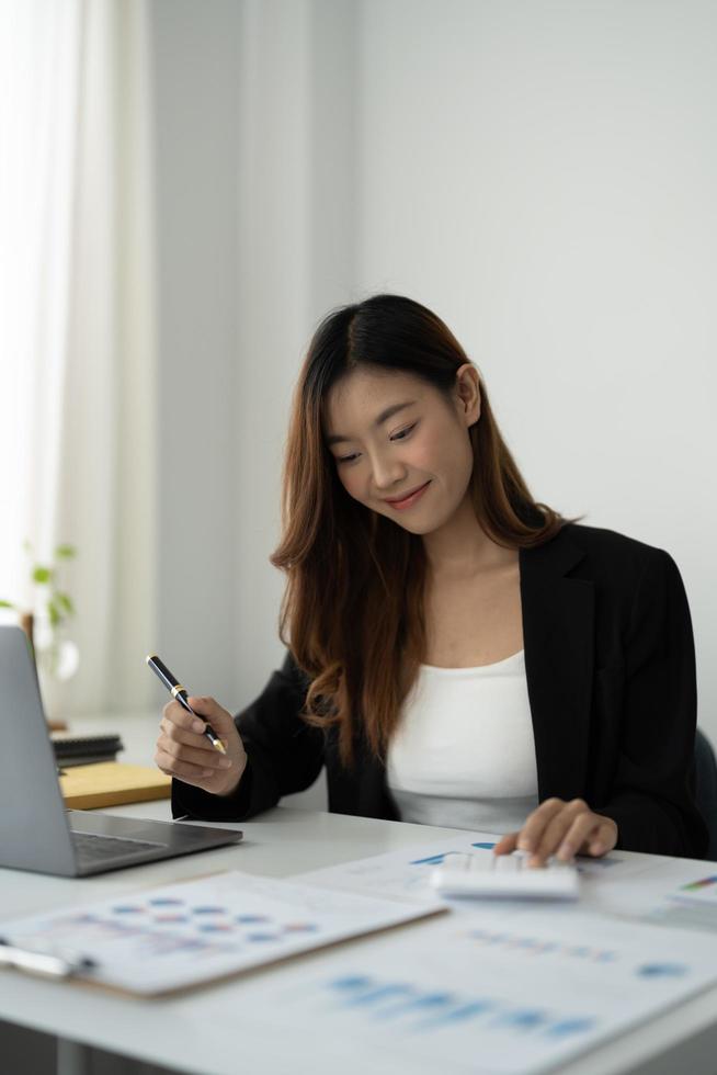 retrato mujer contadora asiática presione a mano en la calculadora para hacer un informe financiero o las ganancias mensuales de la empresa en el escritorio, trabajo de contable y concepto de trabajo desde casa foto