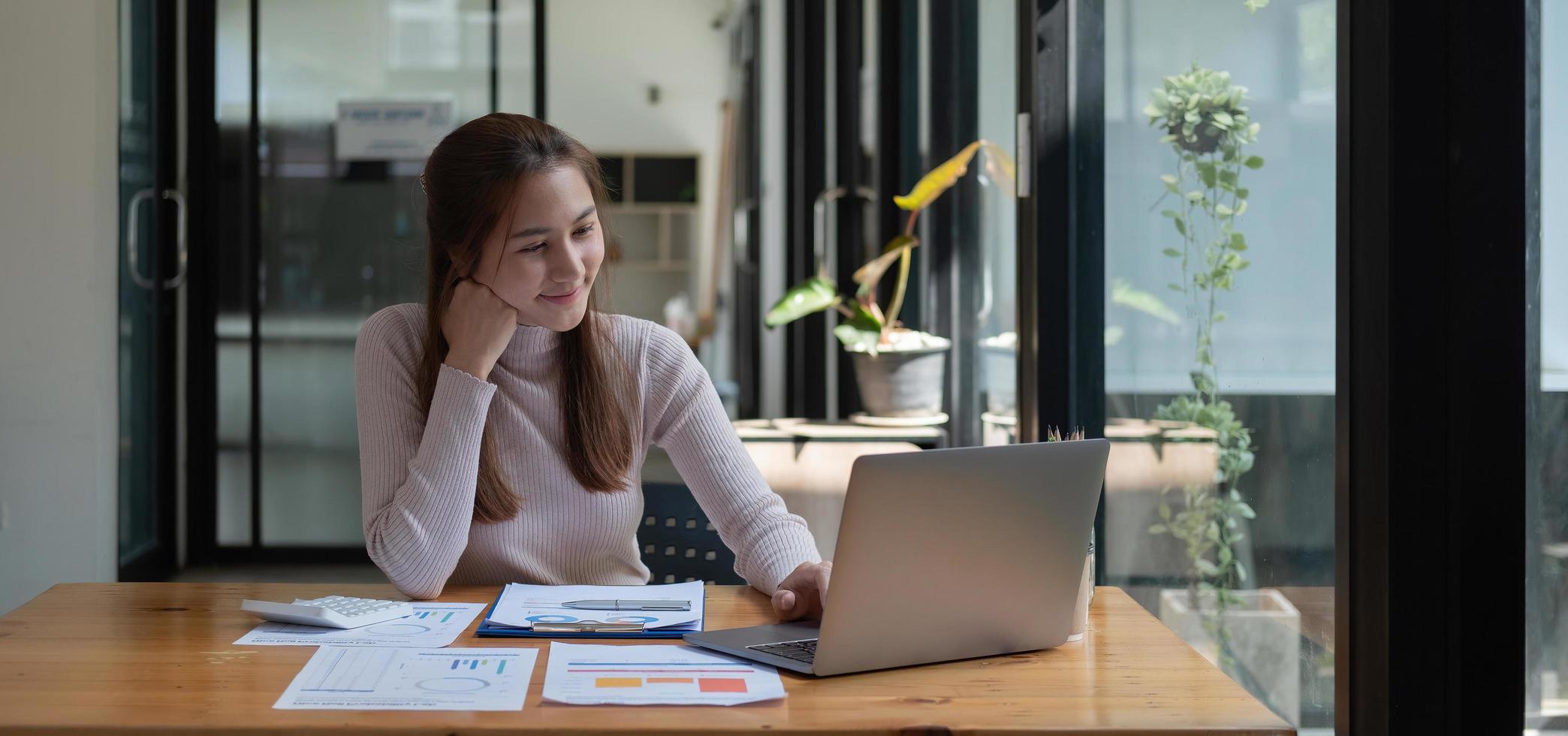 Smiling young asian businesswoman using computer at home office workplace, happy korean employee working on laptop, attractive woman student studying communicating online with laptop computer. photo