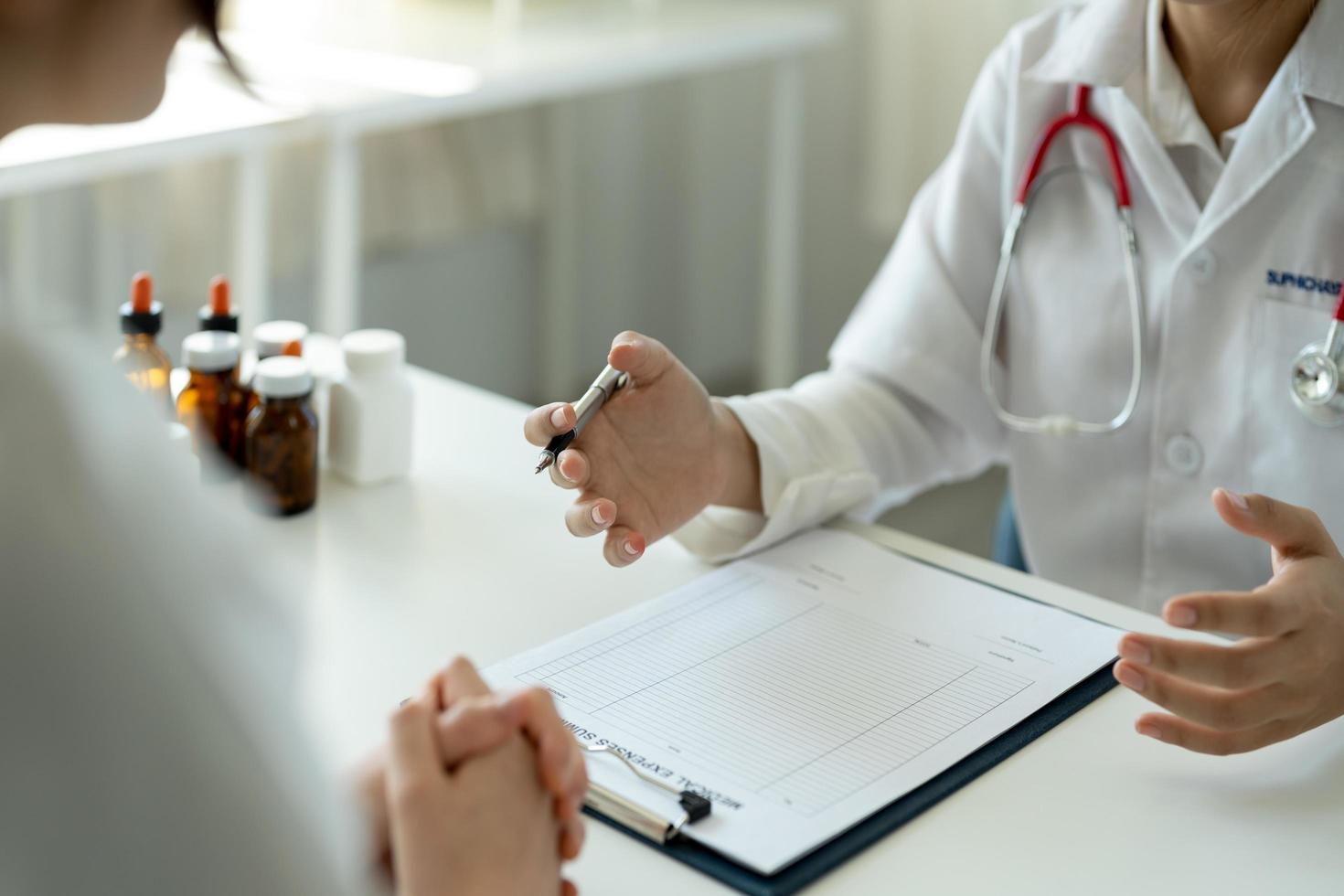 una doctora asiática con uniforme médico blanco consulta a una paciente en un hospital privado. mujer terapeuta habla con mujer cliente en consulta en clínica foto