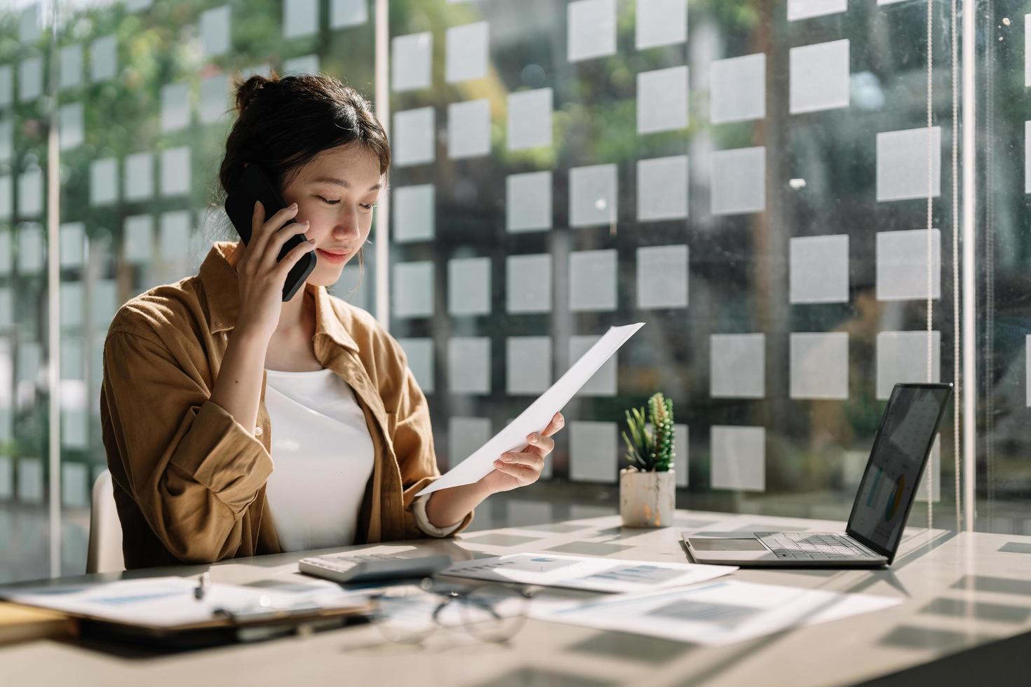 Young asian accountant calling marketing consultants and using laptop computer to analyze sales growth in the global workplace market. accounting concept photo