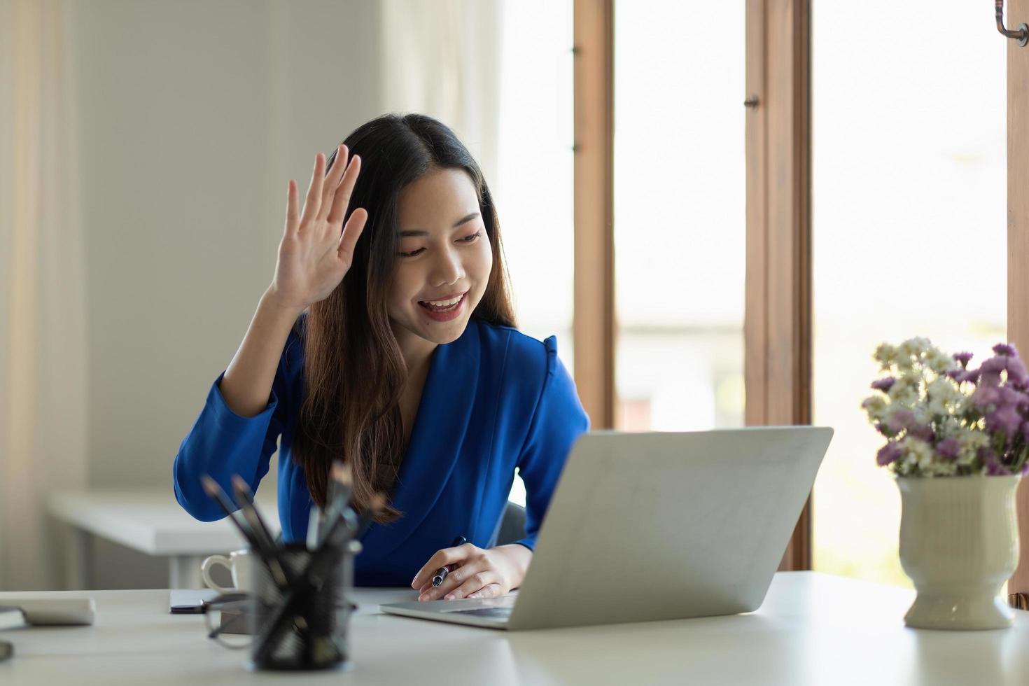 Asia businesswoman using laptop talk to colleagues about plan in video call while smart working from home at living room. Self-isolation, social distancing, quarantine for corona virus prevention photo