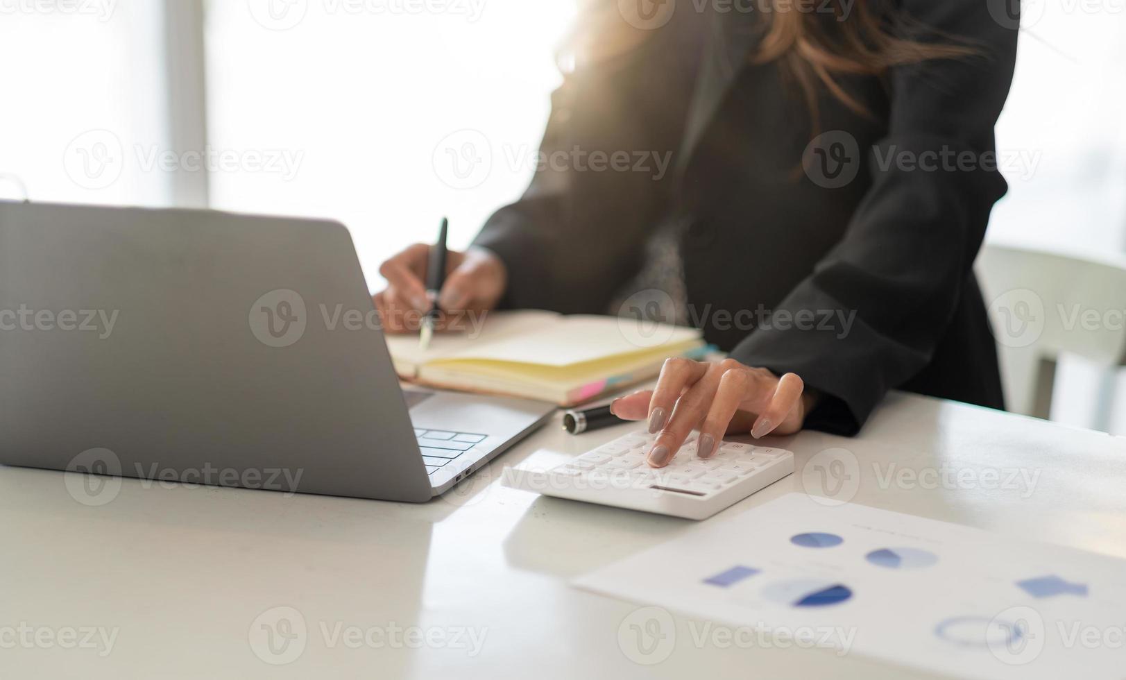 Close up accountant working on desk in office using calculator to calculate budget while taking note on notepad. concept finance and accounting photo
