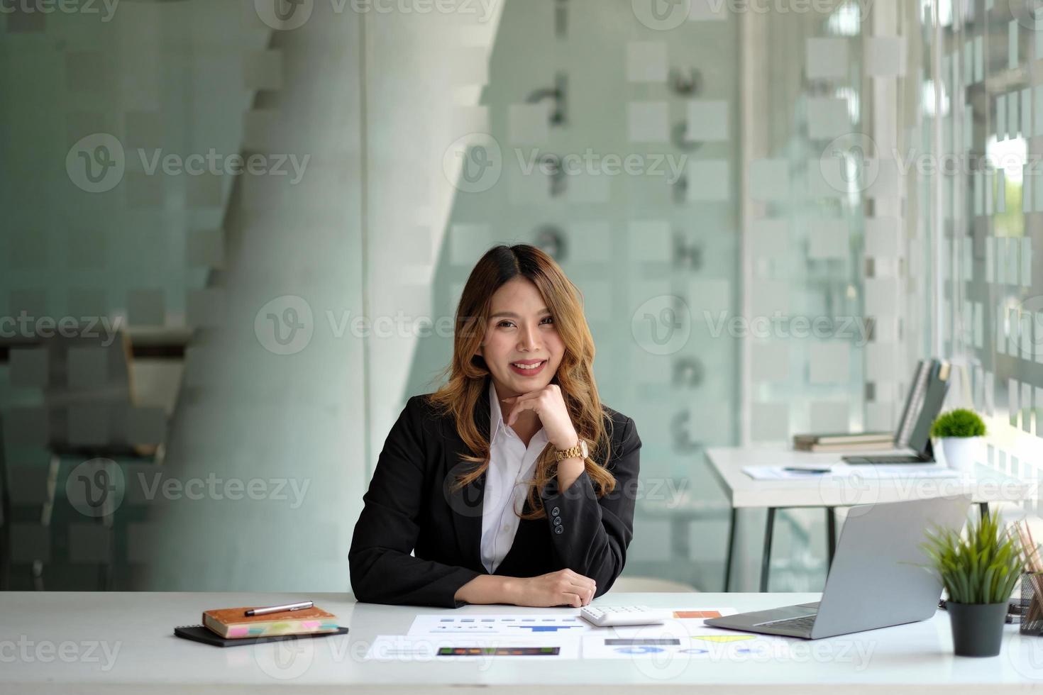 Portrait of attractive business woman sitting at her desk with laptop computer in office. Smiling business woman in black suit at office photo