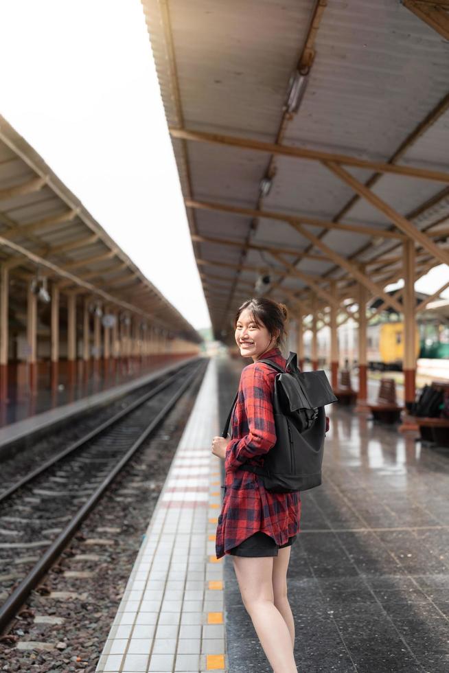 retrato joven mujer asiática mochilero viajero caminando solo en la plataforma de la estación de tren con mochila. mujer asiática esperando el tren en la estación de tren para viajar. vacaciones de verano viajando o joven foto