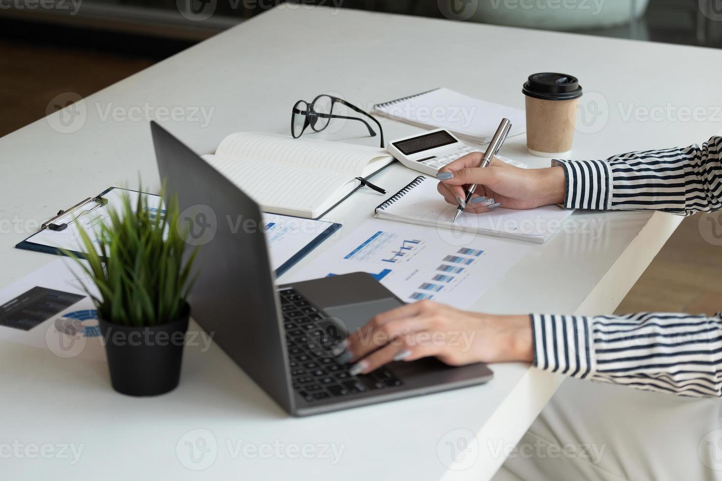 Business women using computer and calculator during note some data on notepad for calculate financial at home office. photo