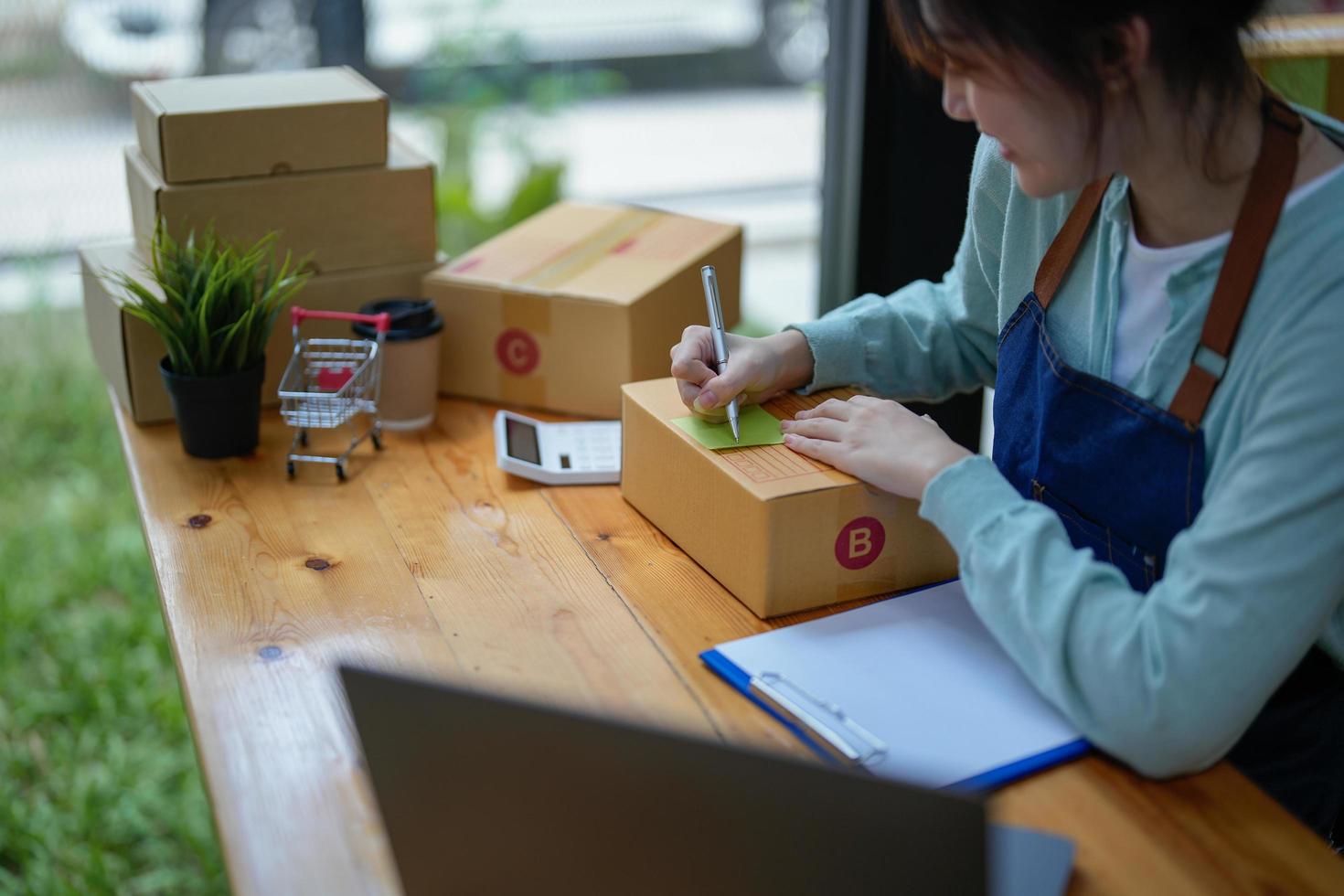 asian entrepreneur working in small start up business online shop company. woman using tape to seal box by packing product to send customers in office. elegant female packaging parcels photo