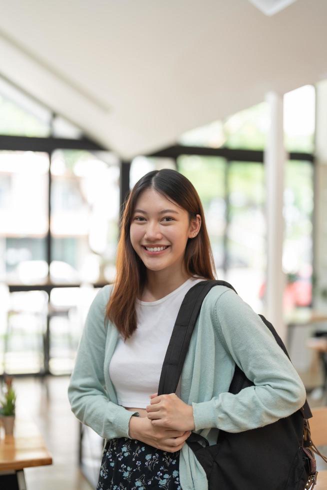 Portrait young asian woman student holding digital tablet at college standing in front of locker with backpack. photo