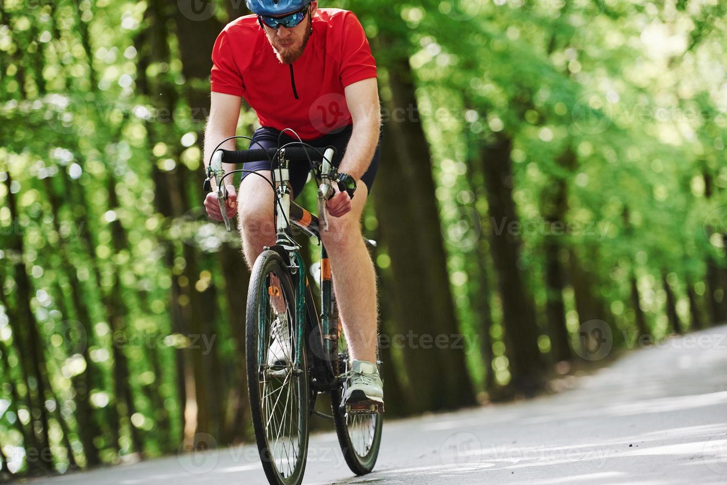 Concentrated look. Cyclist on a bike is on the asphalt road in the forest at sunny day photo