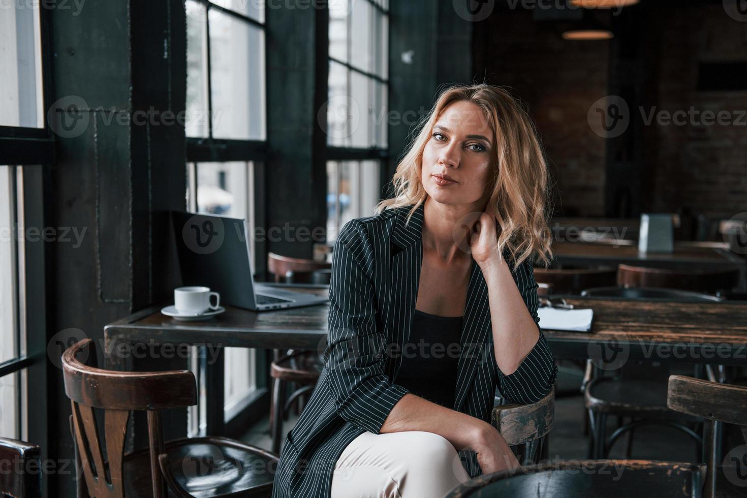 Sitting on the chair. Businesswoman with curly blonde hair indoors in cafe at daytime photo