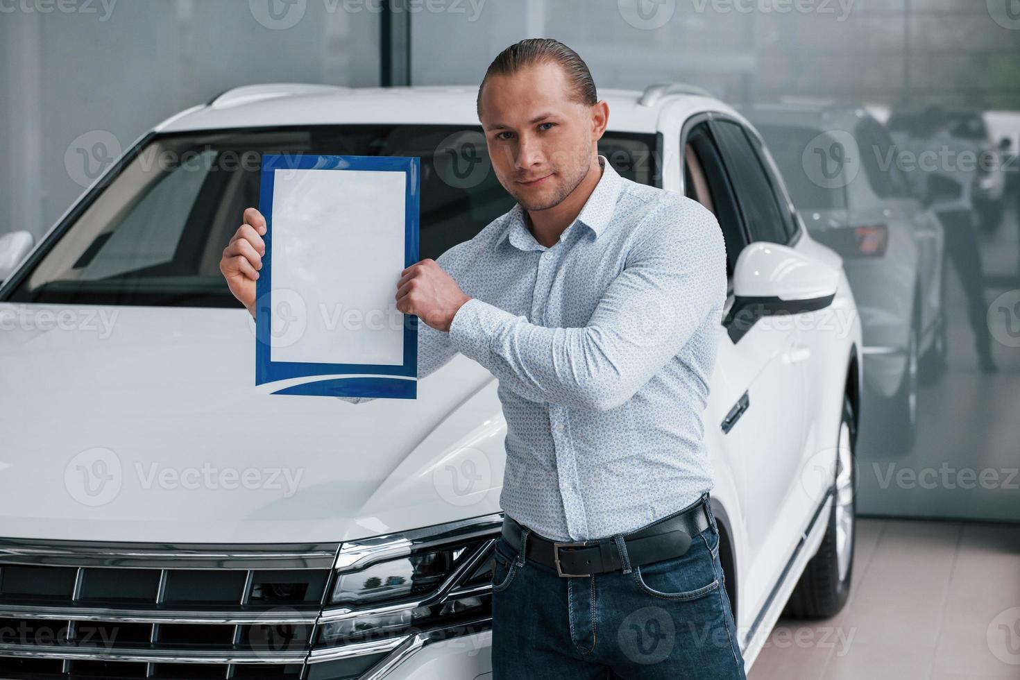 Put your text here. Manager stands in front of modern white car with paper and documents in hands photo