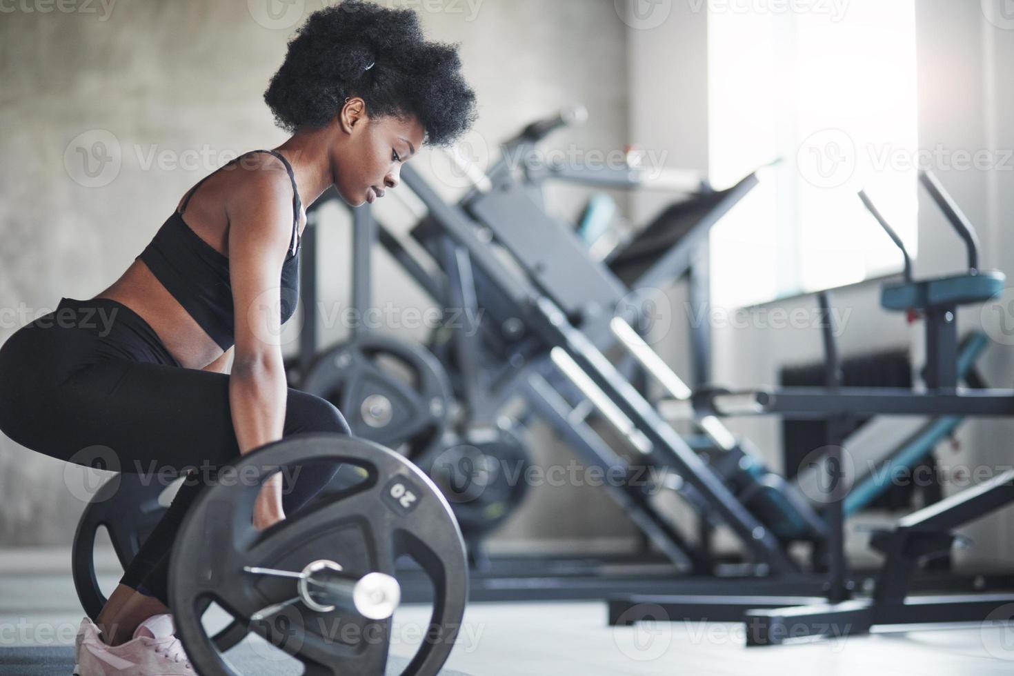 vista lateral. mujer afroamericana con cabello rizado y ropa deportiva tiene un día de fitness en el gimnasio foto