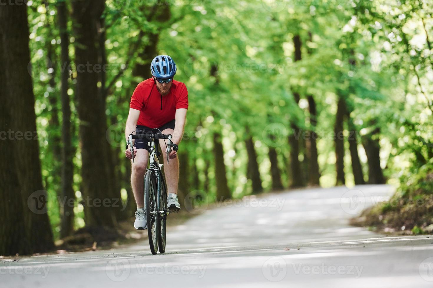 en gafas protectoras. ciclista en bicicleta está en la carretera asfaltada en el bosque en un día soleado foto