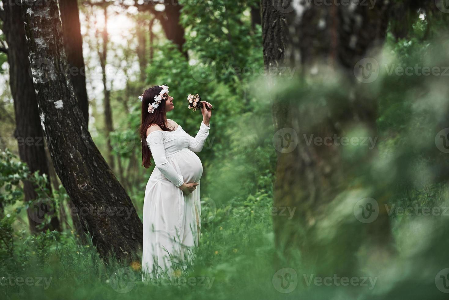 Sunlight and flowers. Beautiful pregnant woman in dress have a walk outdoors. Positive brunette photo