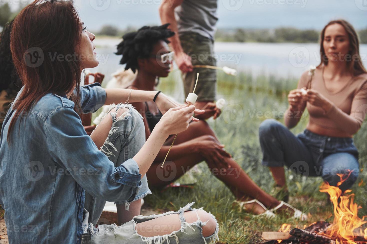 malvaviscos en un palo. grupo de personas hacen picnic en la playa. los amigos se divierten el fin de semana foto