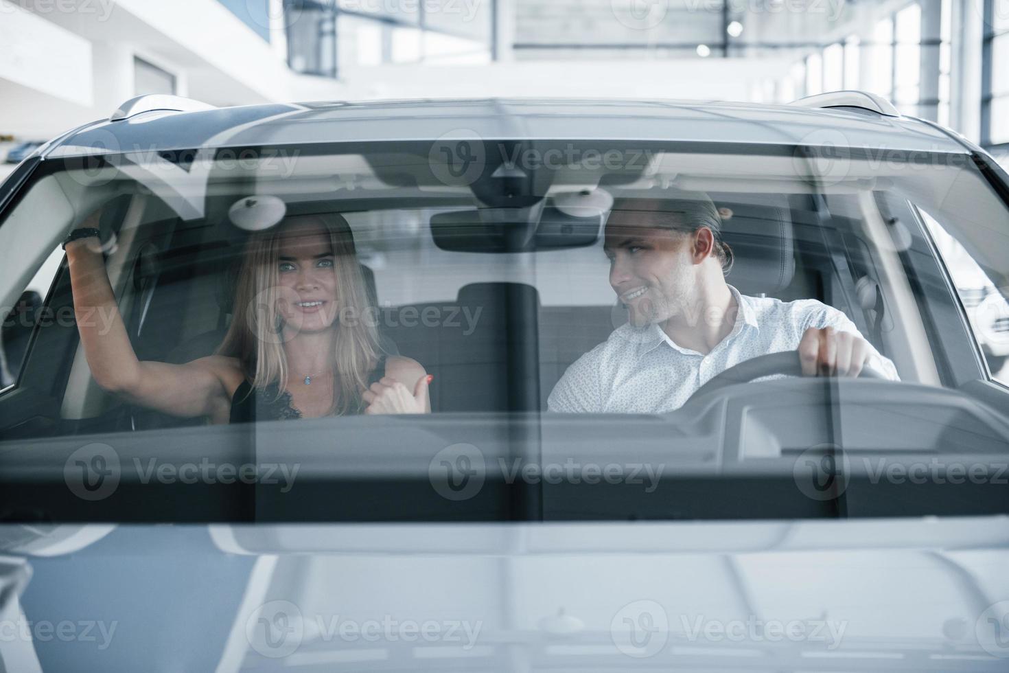 el chico mira a la chica. gerente positivo que muestra las características del nuevo automóvil a una clienta foto